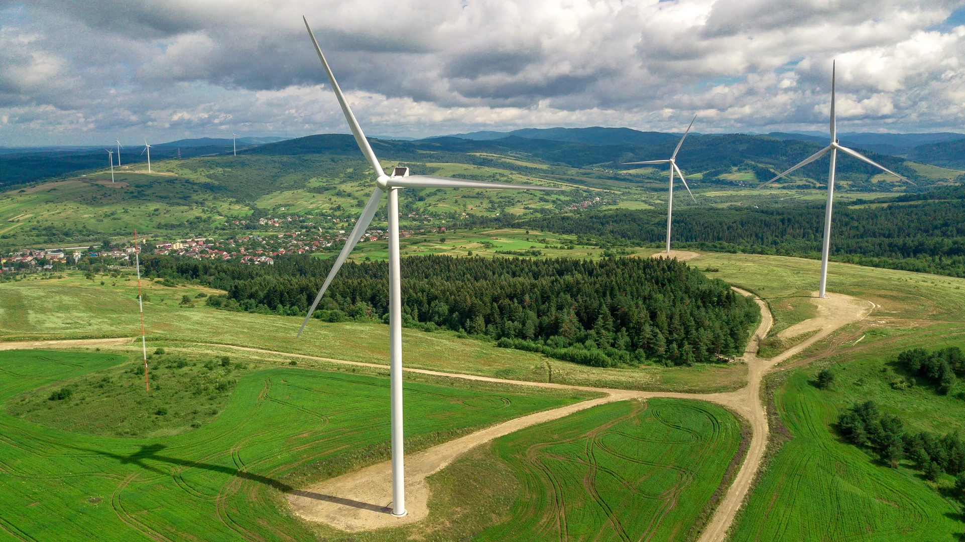 Wind turbines in front of green fields and blue skies with hills in the background