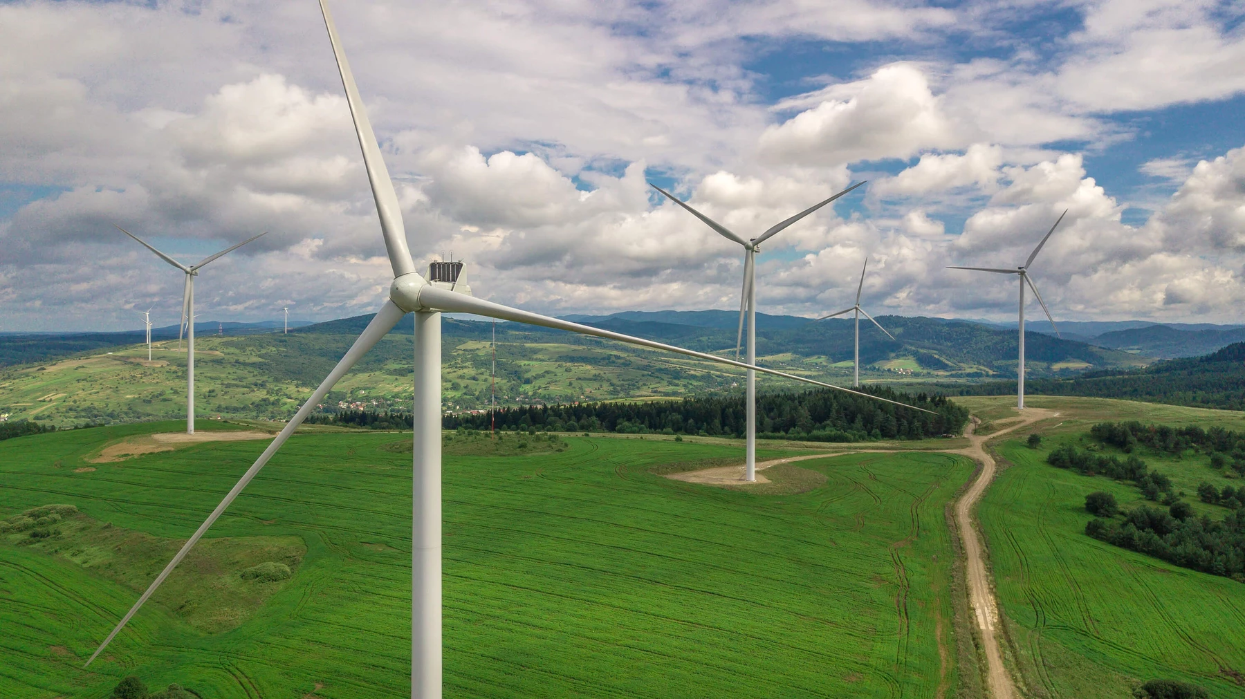 Windräder vor grünen Feldern und blauem Himmel mit Hügeln im Hintergrund
